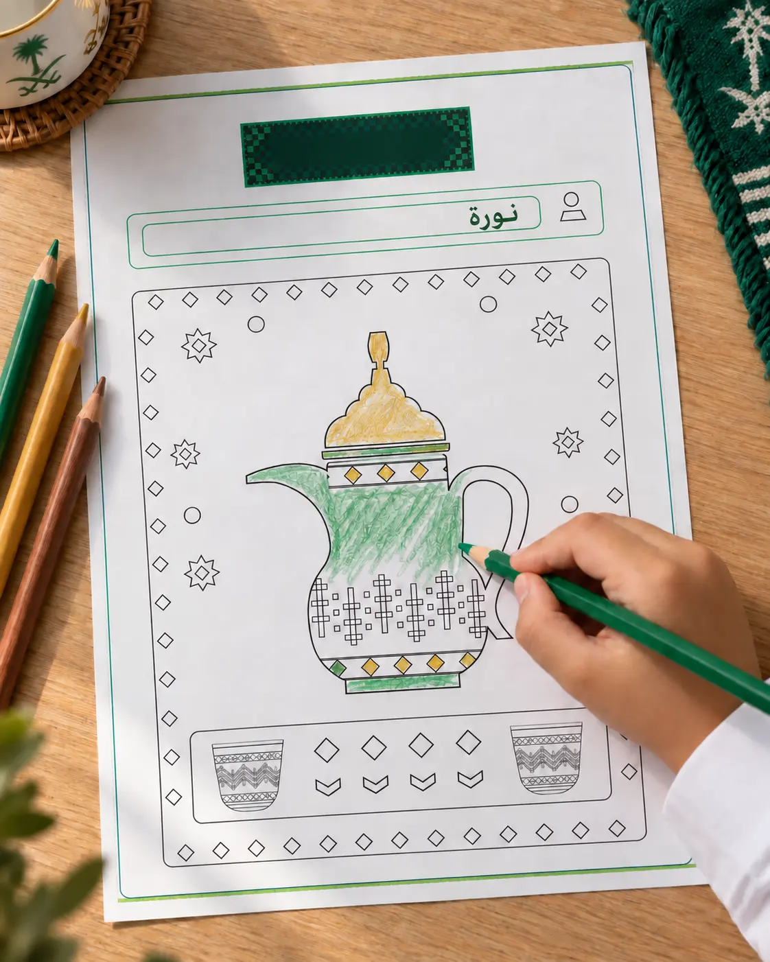 طفل يلوّن صفحة تلوين الدلّة والفناجين بقلم أخضر على طاولة خشبية بجانب أقلام ملوّنة